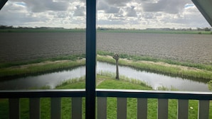 Une vue à travers une fenêtre dont le cadre est en métal, donnant sur un vaste champ et une étendue d’eau.