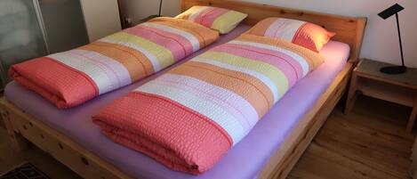 A double bed with a striped blanket and pillows, a wooden headboard, a nightstand with a lamp, and a patterned rug.