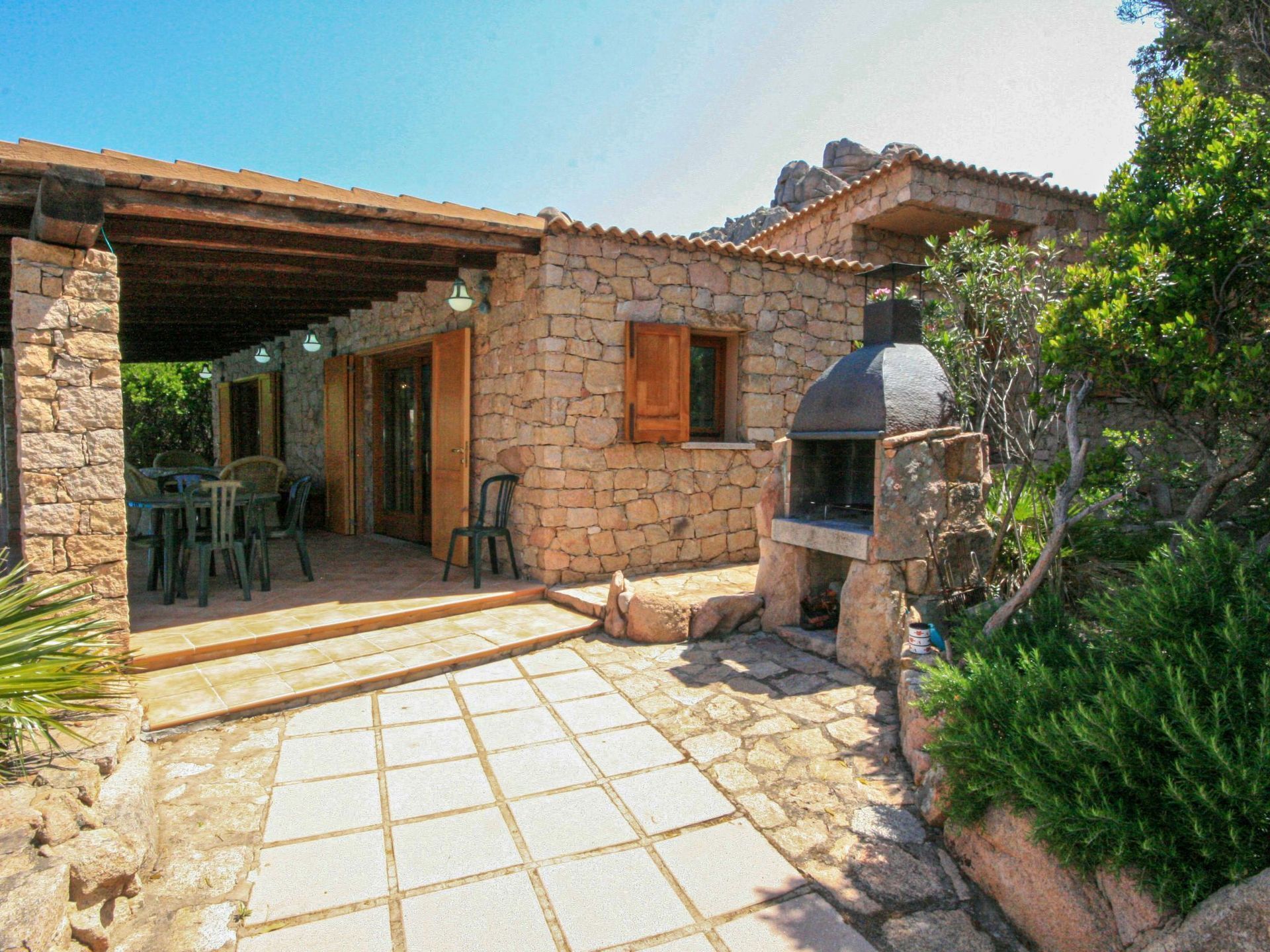 A stone house with a tiled patio, outdoor seating, and a stone chimney.