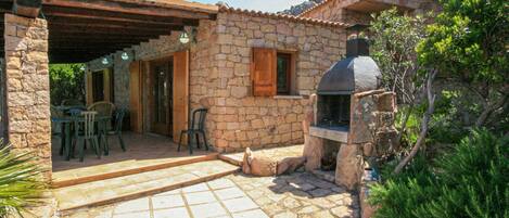 A stone house with a tiled patio, outdoor seating, and a stone chimney.