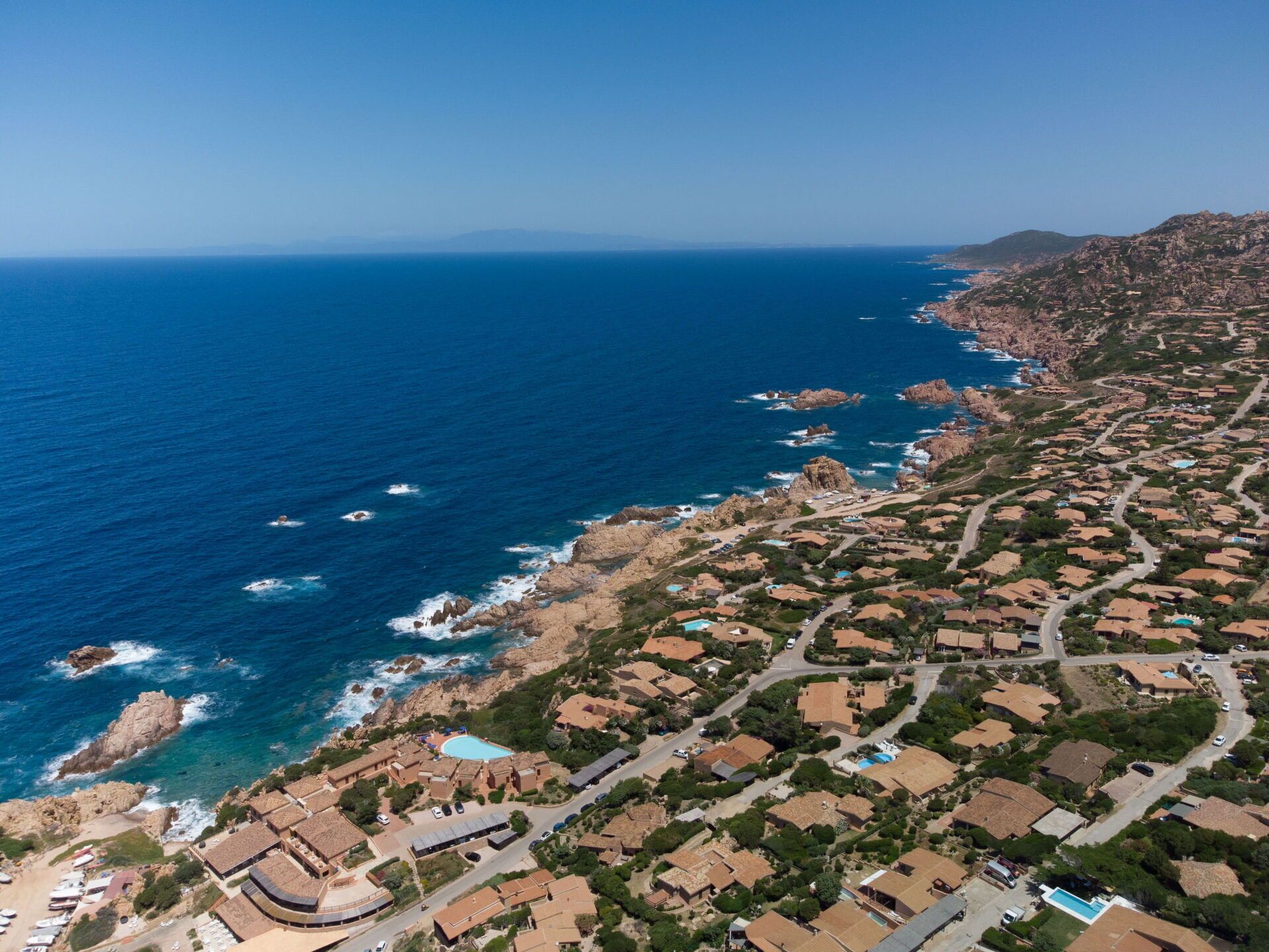 Vista aérea de una zona residencial costera con casas, piscina y costa rocosa.