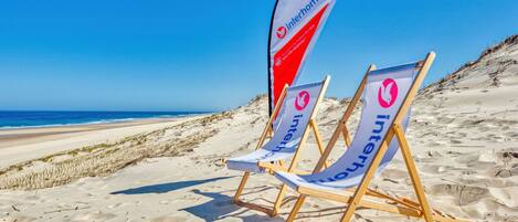Two beach chairs with 'interhome' branding on a sandy beach with a clear blue sky.