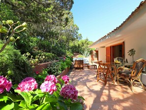 A patio with a table and chairs, surrounded by lush greenery and flowering plants.