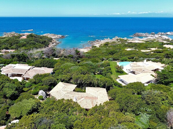 A coastal property with multiple buildings surrounded by lush greenery and rocky terrain.