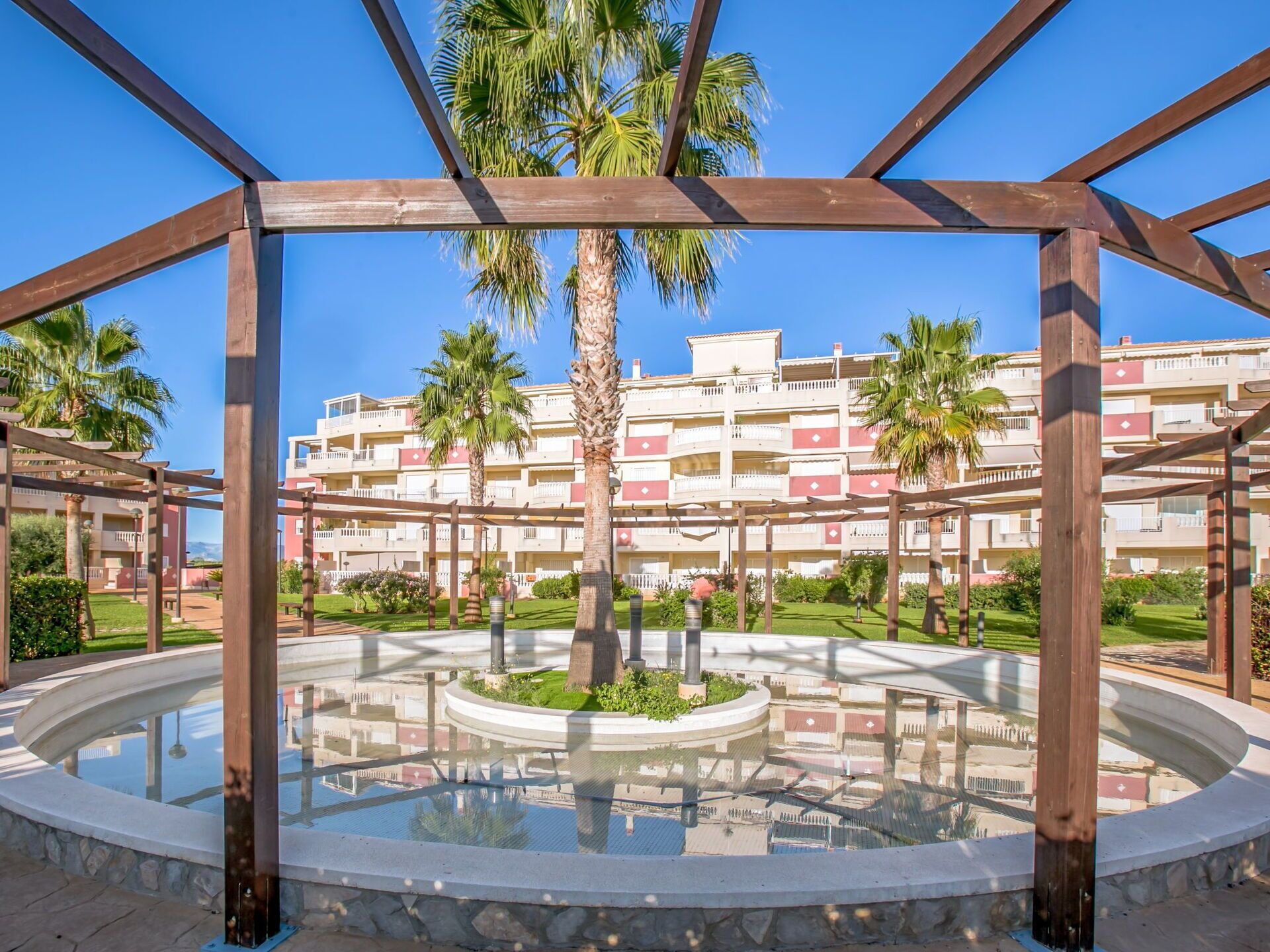 A courtyard with a circular water feature, palm trees, and a multi-story building in the background.
