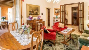 Amplia sala de estar con una mesa de comedor de madera, sillones rojos, una araña y suelo de piedra.