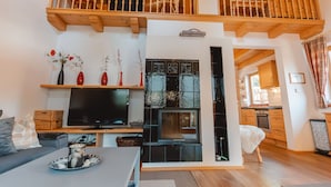 Un salón amplio con techo de madera, televisor, chimenea y balcón.