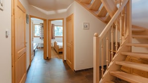 Una escalera de madera que conduce a un segundo piso, un pasillo con puertas de madera y un banco al fondo.