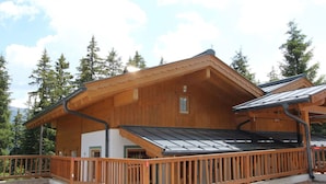 Una cabaña de madera con techo inclinado, un balcón y vistas del bosque circundante.