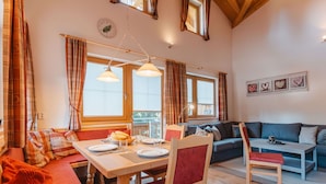 Una sala de estar acogedora con una mesa de comedor de madera, sillas tapizadas en rojo, un sofá azul y techo de madera.