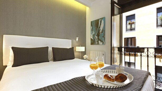 Een hotelkamer met een groot bed, een dienblad met croissants, glazen sinaasappelsap en een kop koffie.