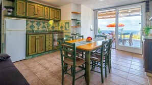 Una cocina con gabinetes verdes, una mesa de comedor con sillas y vista al océano a través de un ventanal corredizo.