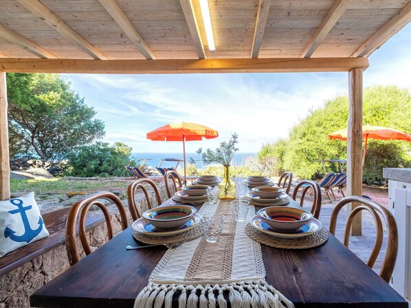 A wooden pergola with a table set for dining, outdoor chairs, and umbrellas.
