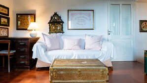A cozy bedroom with a bed, a vintage suitcase, a lamp, and framed pictures on the wall.
