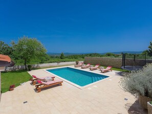 A rectangular pool with a clear blue water, surrounded by a tiled patio with lounge chairs and a table.