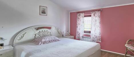 A bedroom with a large bed, a nightstand, a dresser, and a window with floral curtains.