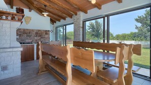 A rustic kitchen with a stone wall, wooden bench seating, and a large window overlooking a garden.