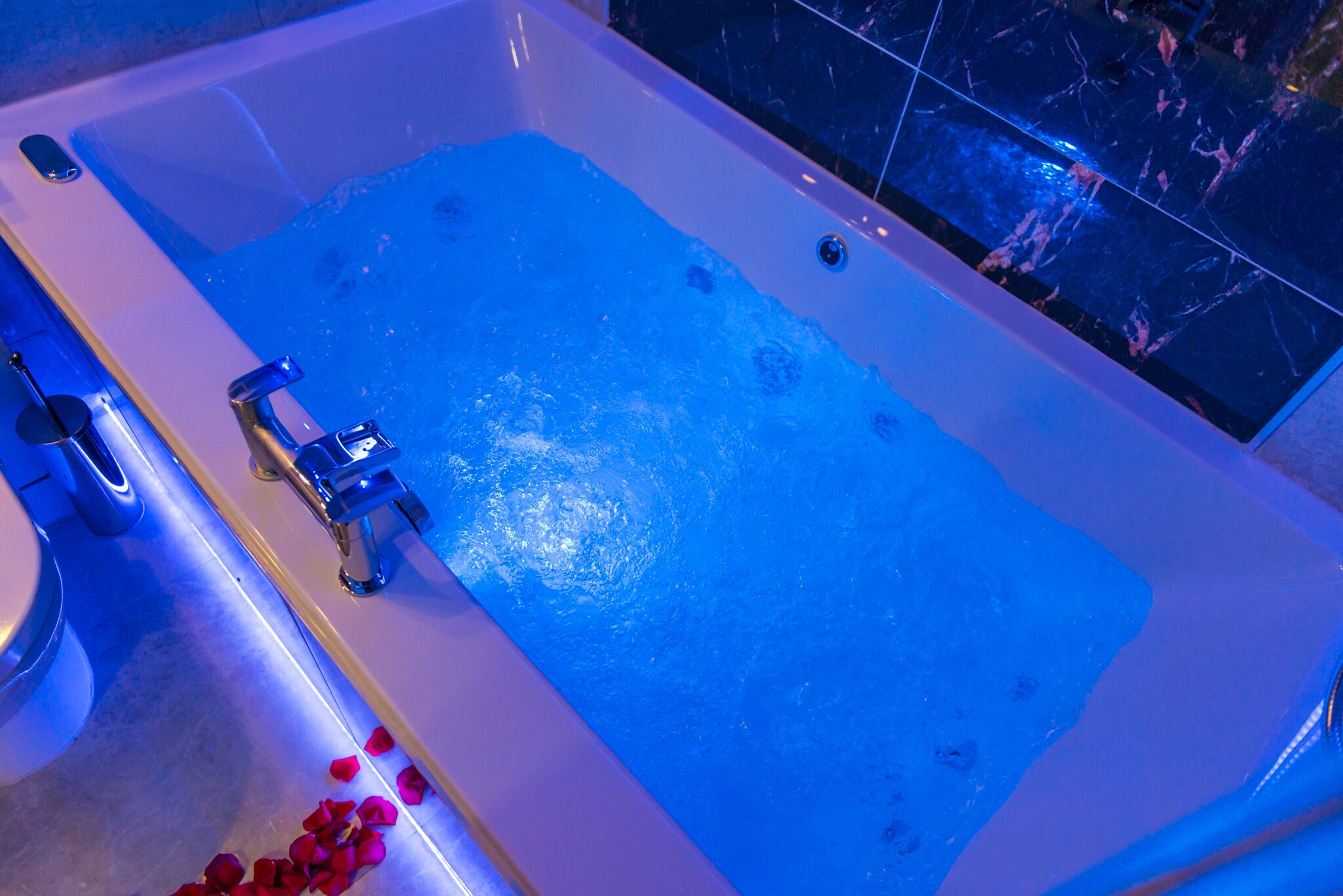 A bathtub with blue lighting, a faucet, and a showerhead.