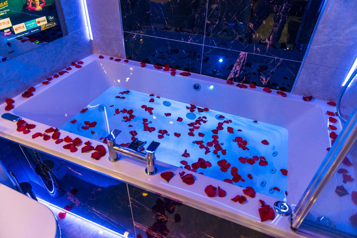 Una bañera llena de pétalos de rosa y una pantalla digital que muestra varios logotipos.