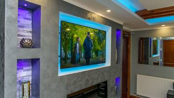 Ein modernes Wohnzimmer mit einem großen Flachbildfernseher an einer strukturierten Wand, einem Kamin darunter und eingebauten Regalen mit dekorativen Gegenständen.