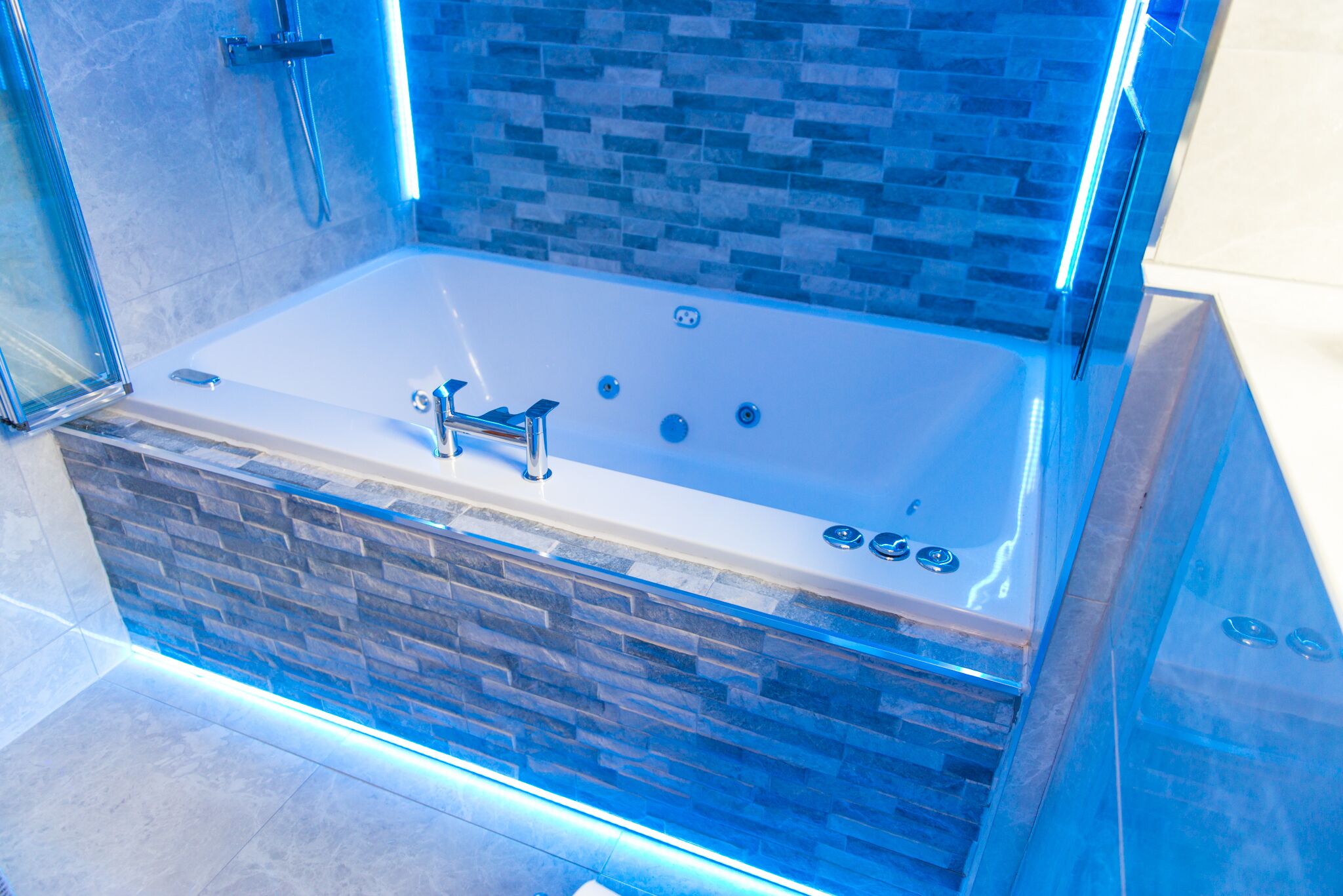 A modern bathroom with a glass-enclosed jacuzzi, stone accents, and a tiled shower area.