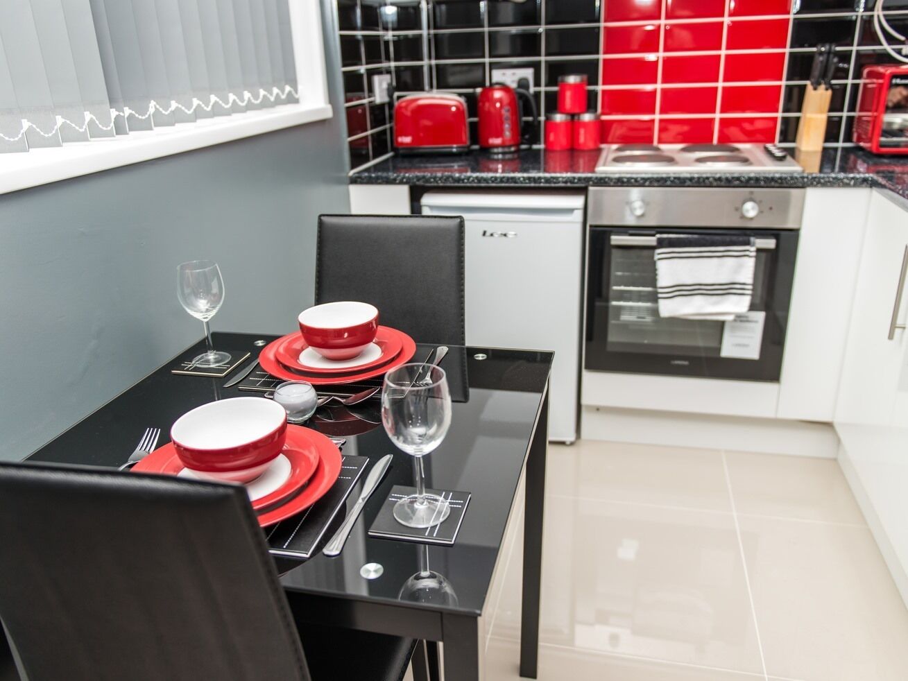Une cuisine moderne avec des appareils électroménagers rouges, une table à manger dressée pour deux personnes et un petit réfrigérateur.
