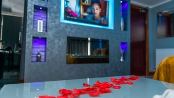 A modern interior with a glass table displaying red rose petals, a mounted TV, and ambient lighting.
