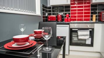 A modern kitchen with red and white appliances, a black dining table set with red plates and a wine glass, and a view of the kitchen area.