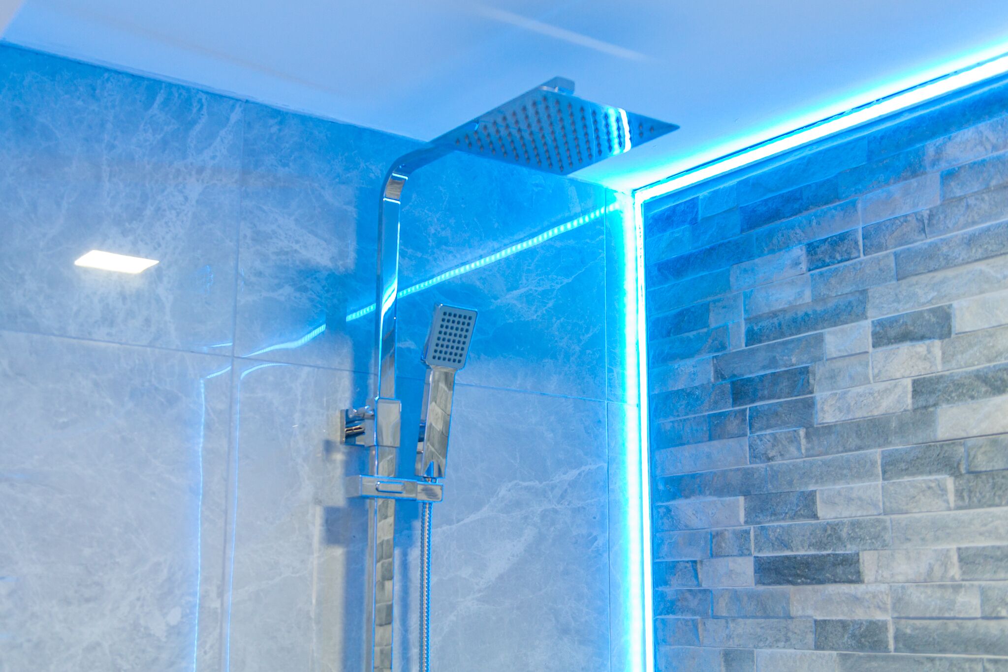A modern shower with a glass enclosure and blue LED lighting.