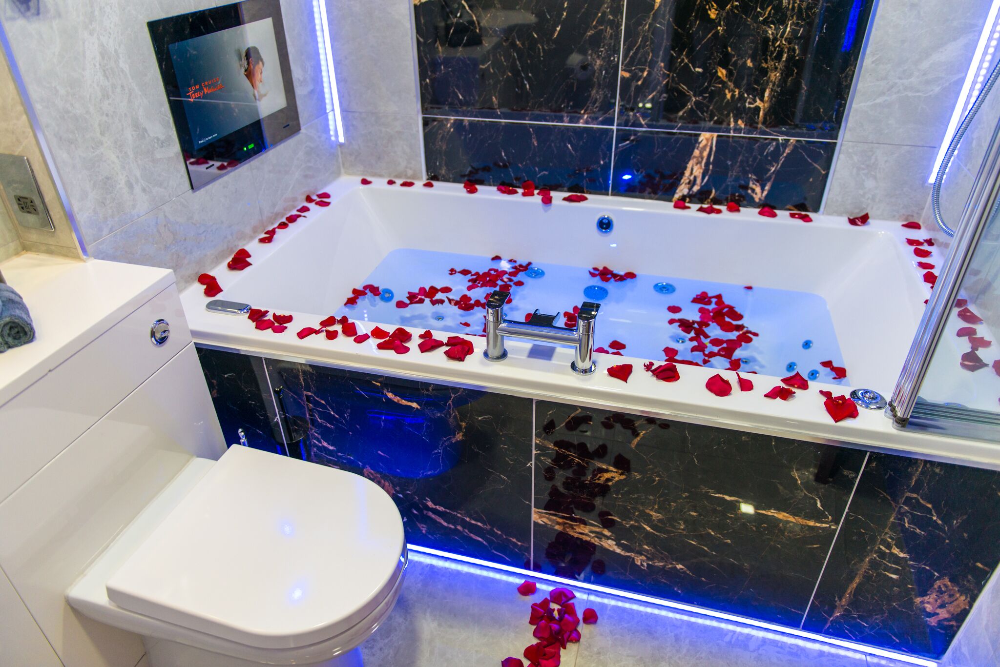 Ein modernes Badezimmer mit einer Badewanne, gefüllt mit Rosenblättern, einer Toilette und einer Wand mit Marmorfliesen.