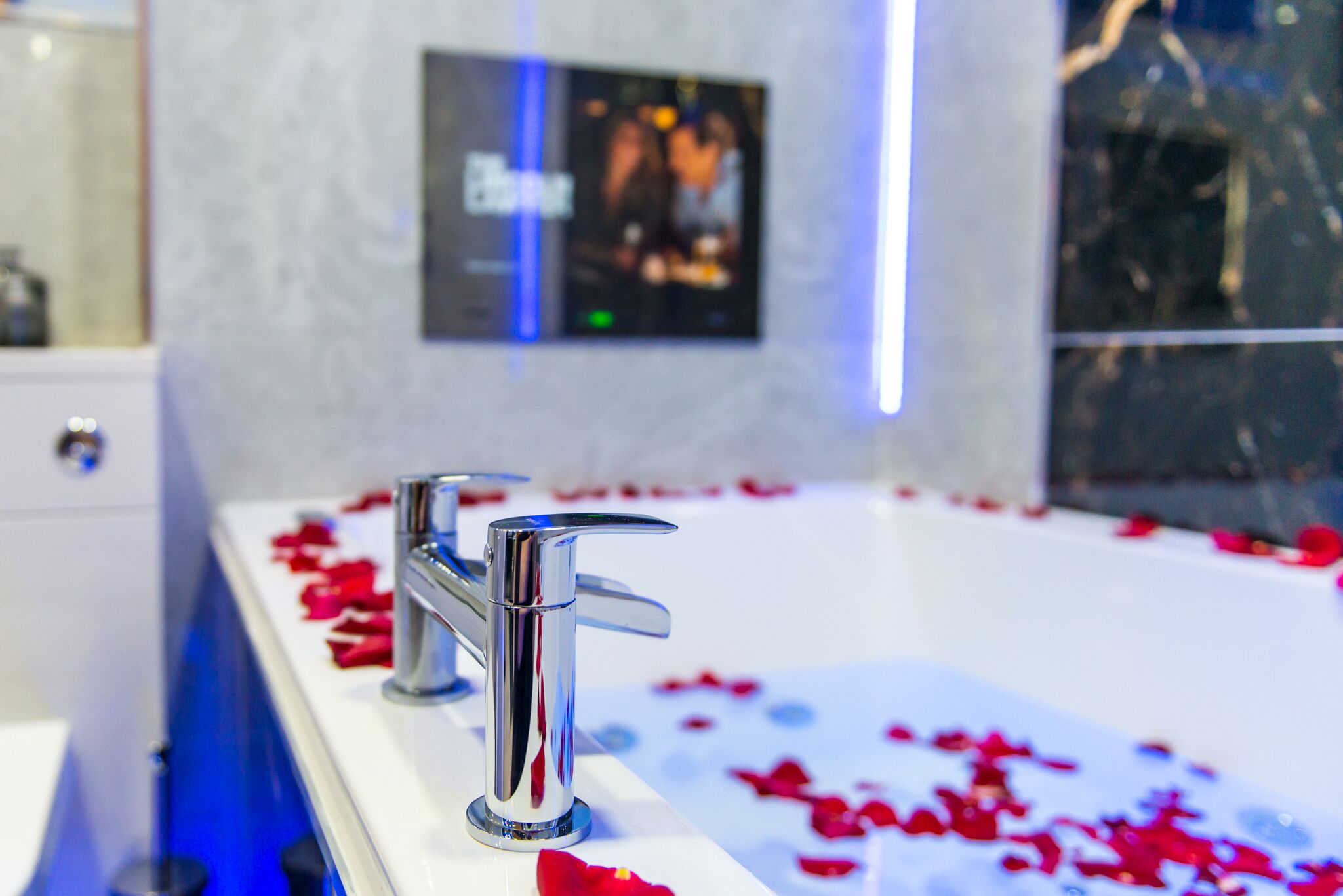 Ein modernes Badezimmer mit einer großen Badewanne, chromfarbenen Armaturen und Rosenblütenblättern auf dem Boden.