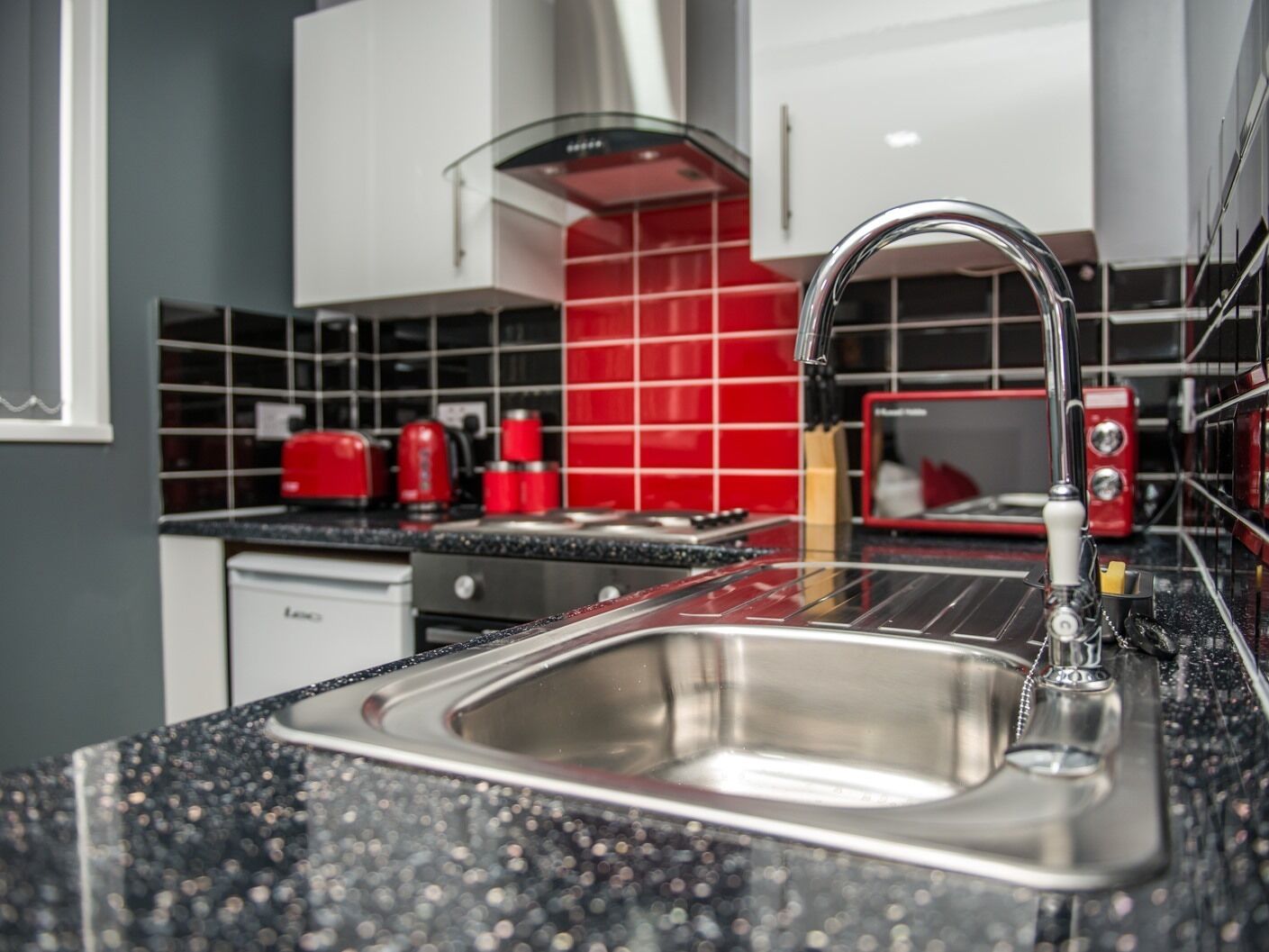 Una cocina moderna con un lavamanos de acero inoxidable, electrodomésticos rojos y encimeras con motas negras.