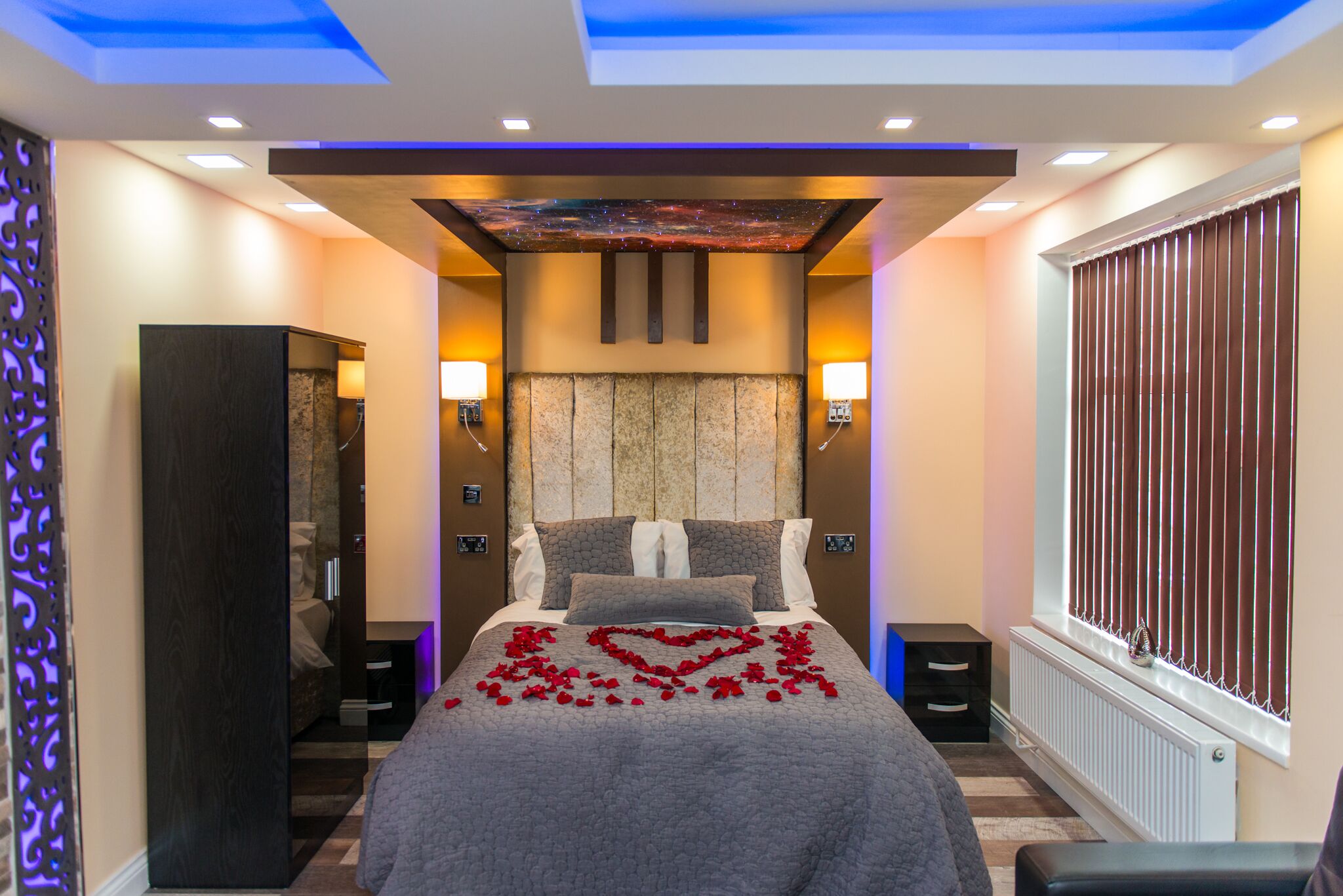 A modern bedroom with a large bed, a decorative ceiling, and a window with blinds.