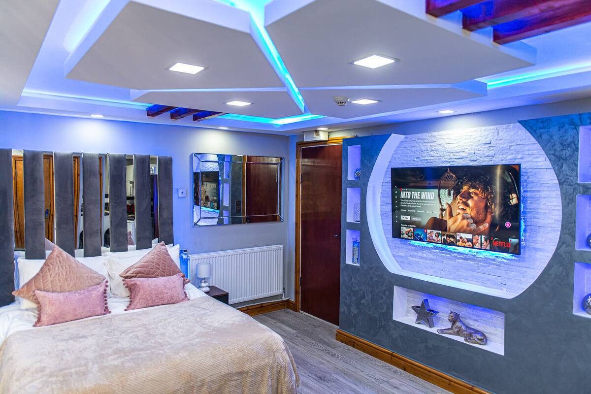 Una habitación de hotel moderna con una cama grande, un televisor montado en la pared y un diseño de techo original.