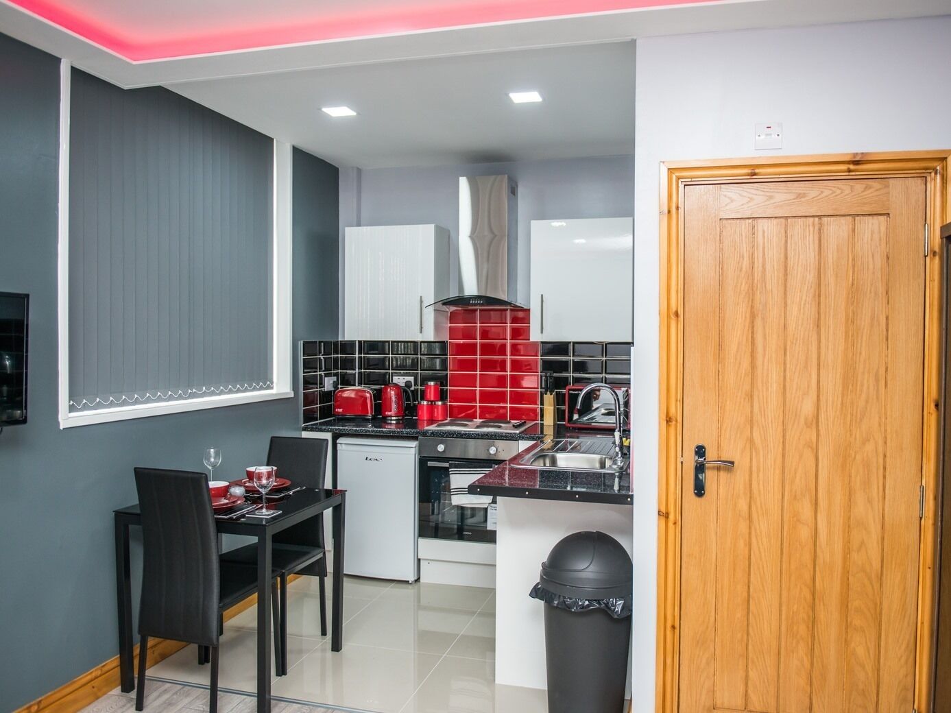 A compact kitchen with a dining area, featuring a black countertop, red appliances, and a wooden door.