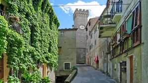 A narrow street with buildings on either side, one with a clock tower in the background. - Beautiful private villa for 2 people with WIFI, A/C, TV, patio, pets allowed and panoramic view (Roccastrada)