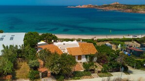 A coastal property with a beach view, white buildings with orange roofs, and a rocky outcrop in the distance. - Cosy apartment for 3 guests with patio and pets allowed (Trinità D'agultu)