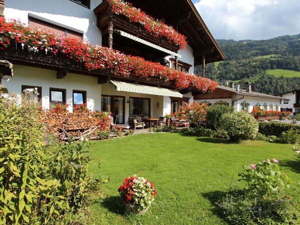 A traditional chalet with a well-maintained garden, outdoor seating, and a scenic mountain backdrop.