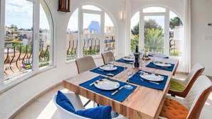 A dining area with a wooden table set for six, large arched windows, and a view of the cityscape.