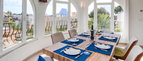 A dining area with a wooden table set for six, large arched windows, and a view of the cityscape.