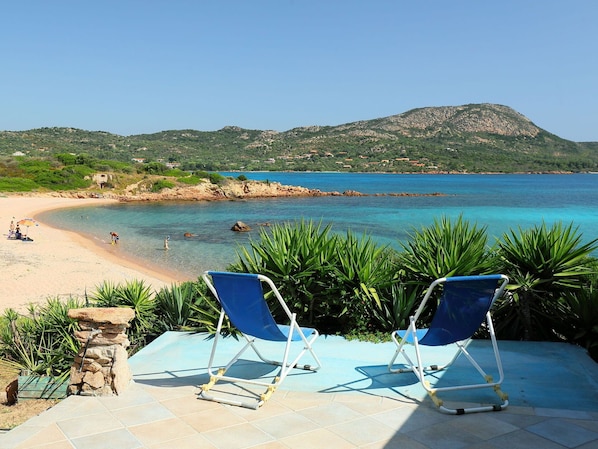 A beach with clear blue waters, two blue lounge chairs, and a stone pillar.