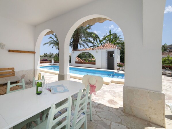 Un espace extérieur avec une piscine, une table et des chaises, un banc et une petite construction dotée d’un toit en tuiles.