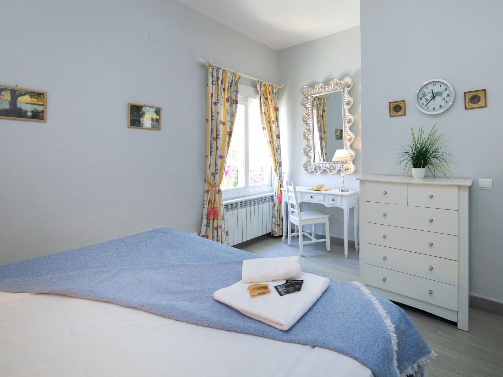 Un dormitorio con cama, escritorio, cómoda, espejo y ventana con cortinas.