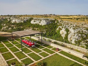 An outdoor dining area with a red table and chairs, surrounded by a stone wall and lush greenery. - Stunning private villa for 16 guests with WIFI, A/C, private pool, hot tub, TV and patio (Modica)