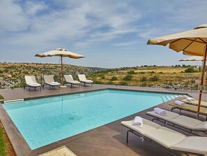 A swimming pool with lounge chairs and umbrellas, surrounded by a scenic hillside view. - Stunning private villa for 16 guests with WIFI, A/C, private pool, hot tub, TV and patio (Modica)
