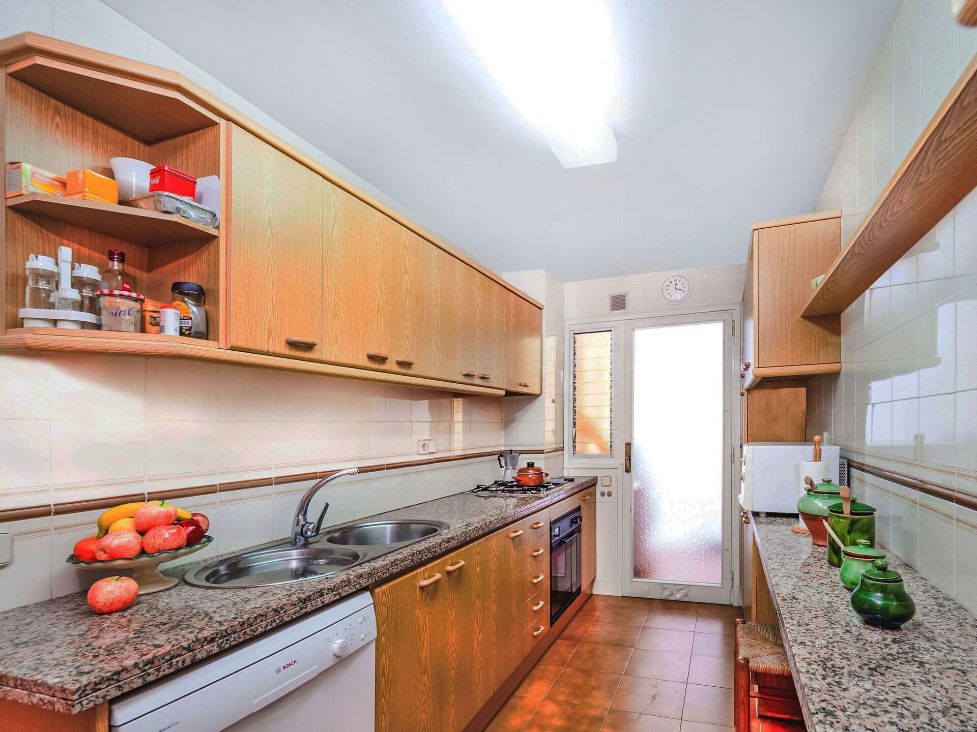 A compact kitchen with wooden cabinets, a granite countertop, a Bosch dishwasher, and a window with frosted glass.
