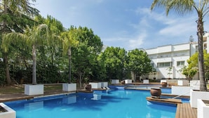 Una piscina con varias secciones, rodeada de macetas blancas y palmeras.
