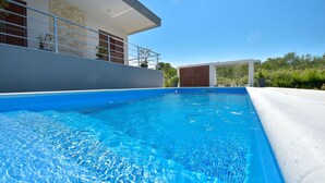 Et moderne poolområde med en klar, blå pool, en hvid bygning med balkon og en trædør.