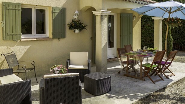 Une terrasse dotée de meubles en osier, d’une table avec des chaises et d’un pot de fleurs suspendu.