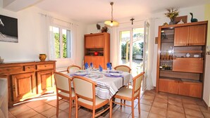 Un coin repas avec une table dressée pour quatre personnes, des chaises en bois, un meuble contenant de l’ustensile de cuisine et une vue sur l’extérieur.